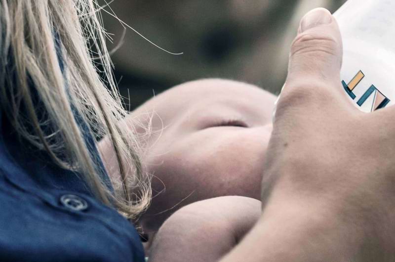 Baby får flaske på mors arm